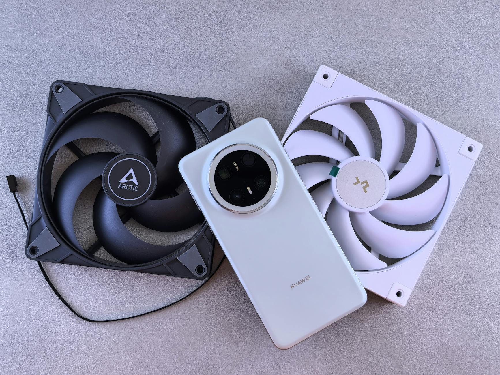 Image of a smartphone alongside two cooling fans on a textured gray surface.
