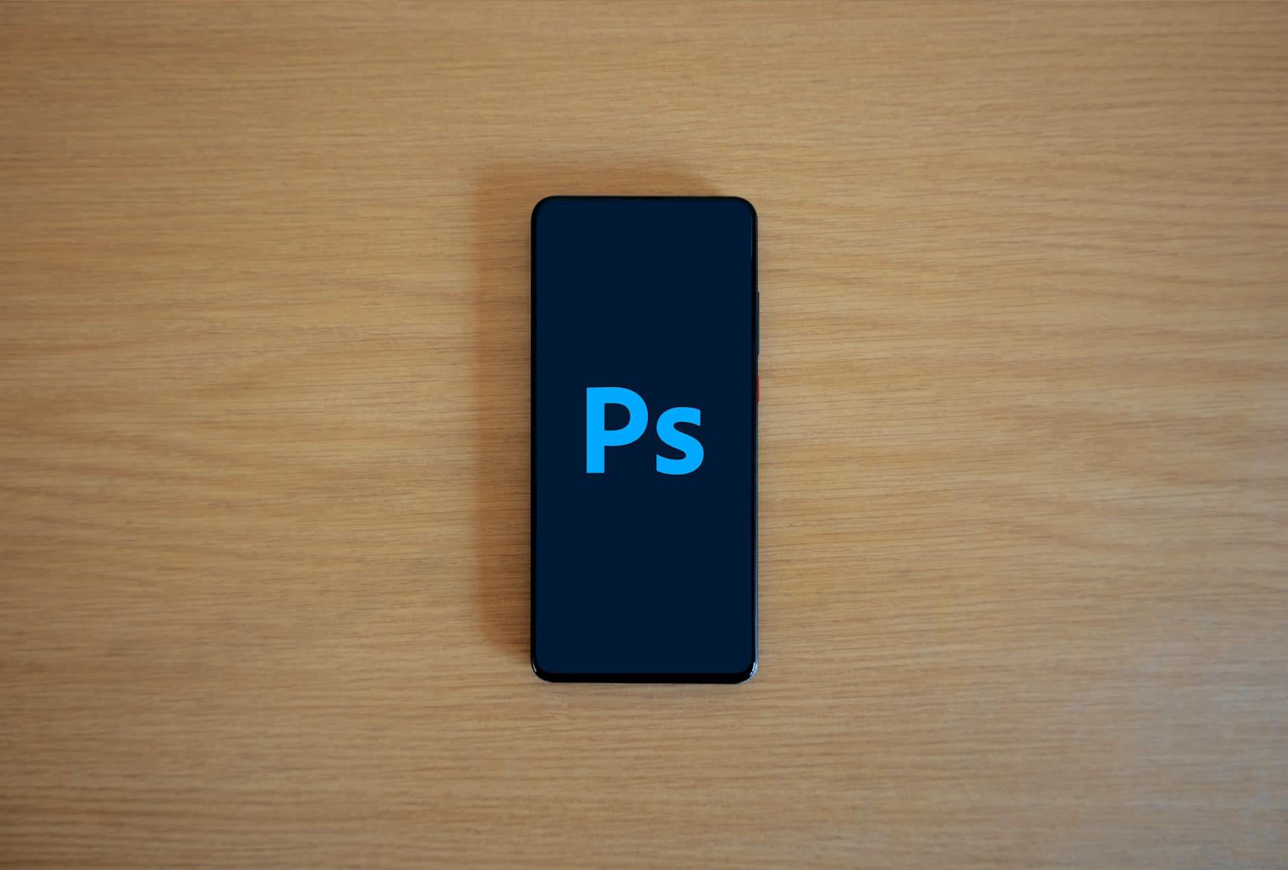Top view of a smartphone showing Adobe Photoshop on a wooden surface.