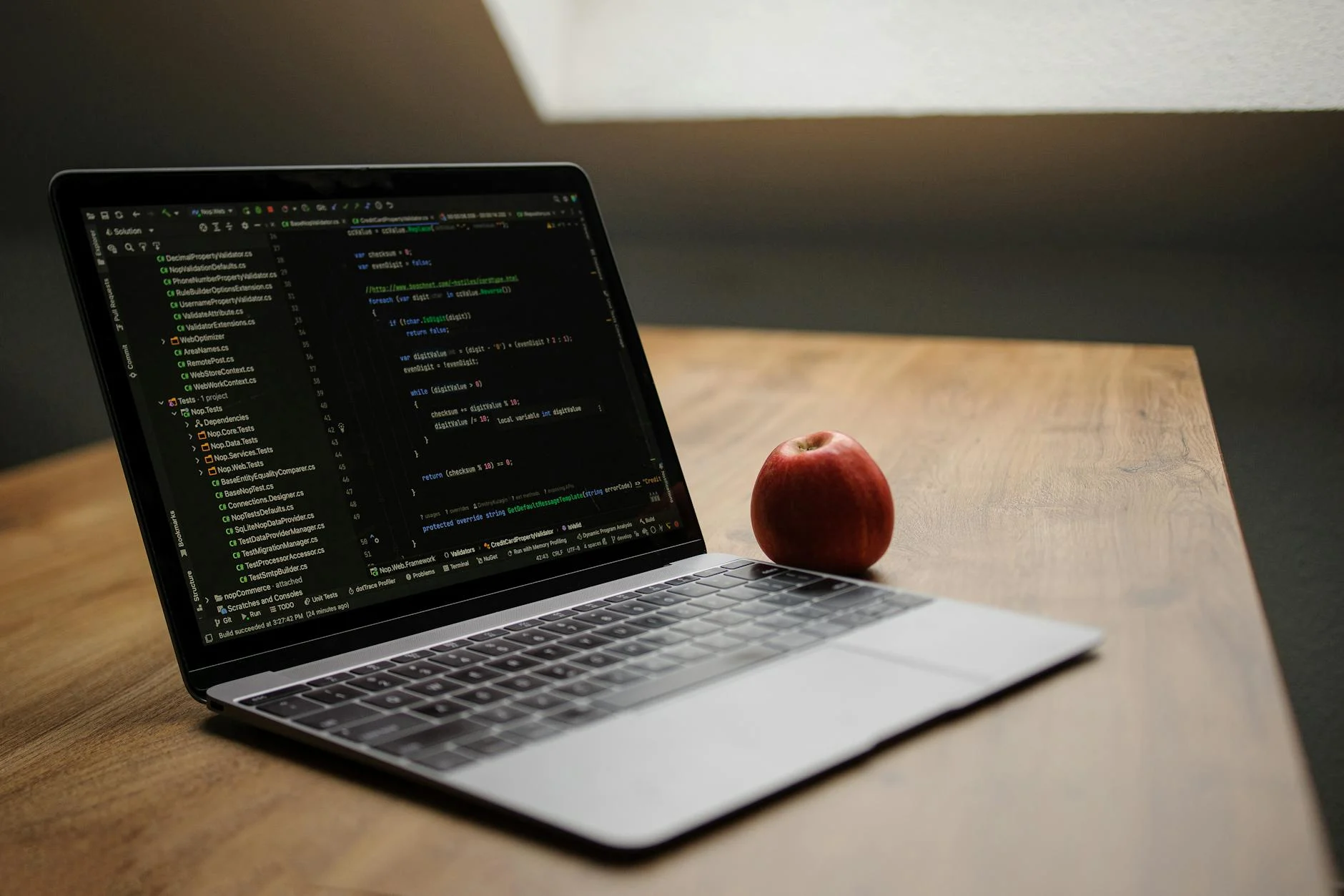 Open laptop displaying code next to a red apple on a wooden desk.