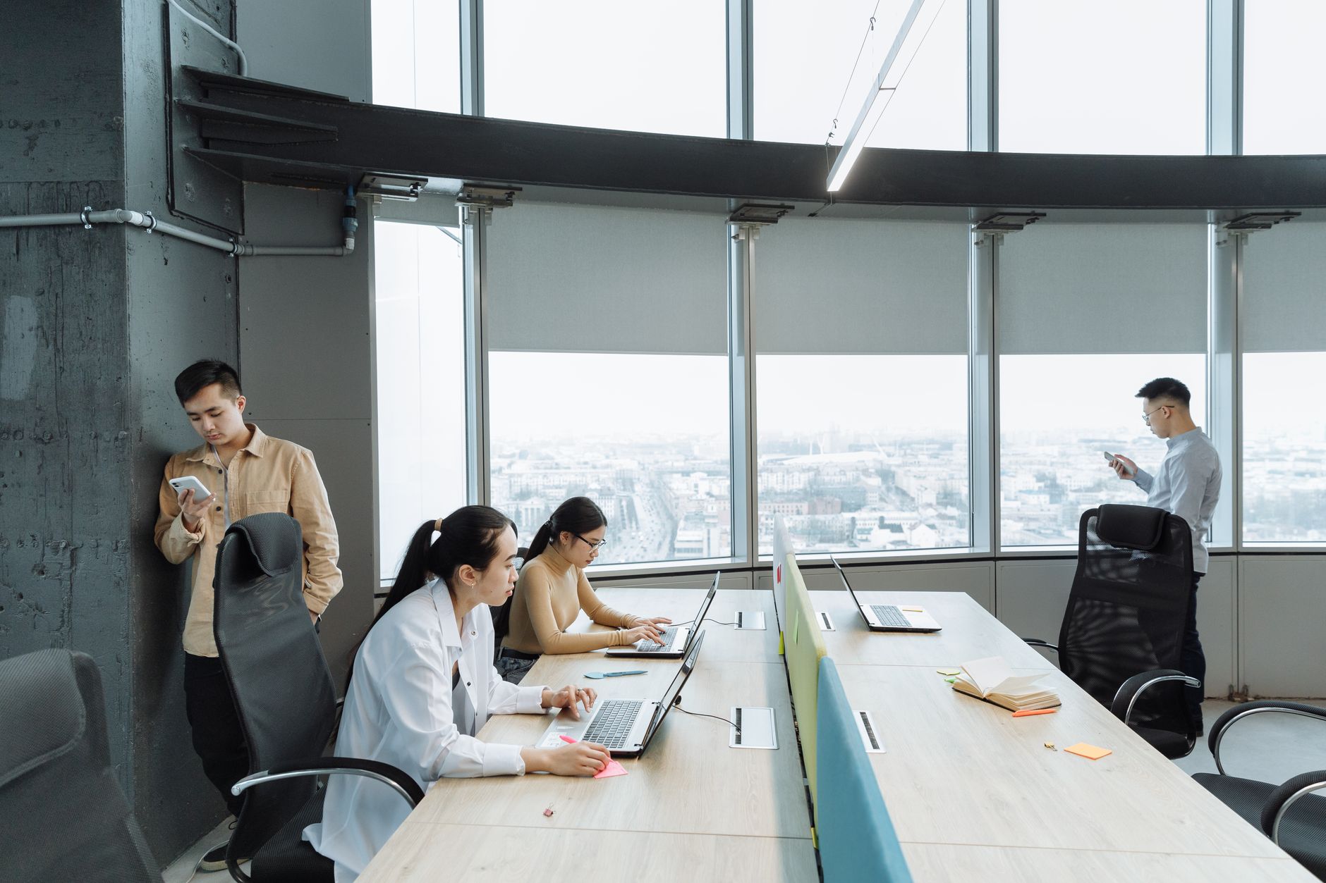 Contemporary office scene with Asian coworkers working on laptops and smartphones.